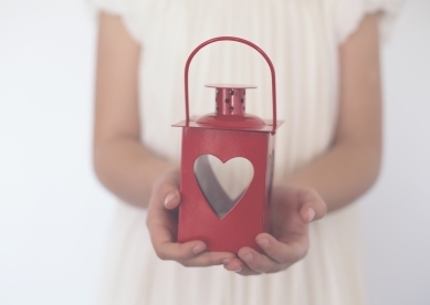 Child's hands holding a red metal lantern with a heart shaped cut out